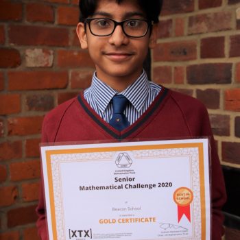school boy wearing glasses and holding a gold certificate for a maths challenge