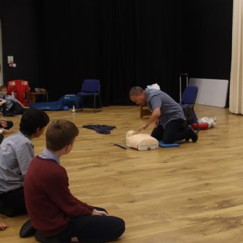 A first aid teacher demonstrates how to give chest compressions to the CPR doll