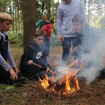 4 boys working on making a fire using kindling in the woods