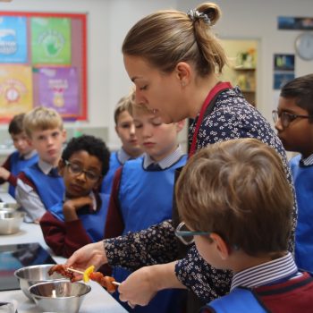Teacher lines up kebab sticks ready to be cooked while students look on