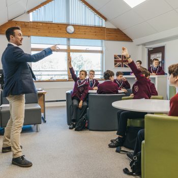 Teacher talking to a student as he raises his hand